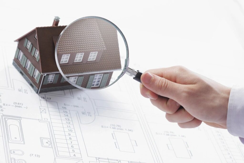 House model on blueprints with magnifying glass, representing roofing company services in Los Angeles.