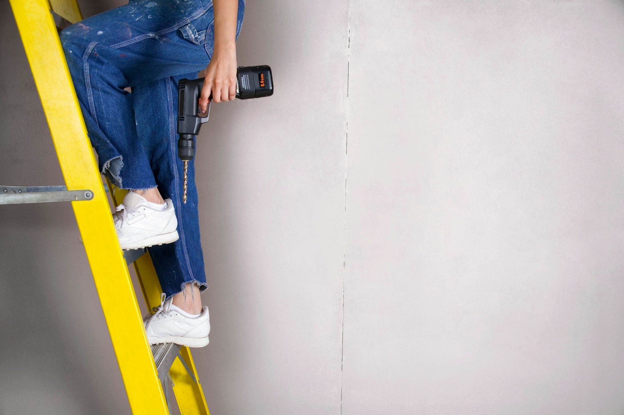 Person on ladder with drill for roof repairs and installation services in Los Angeles.